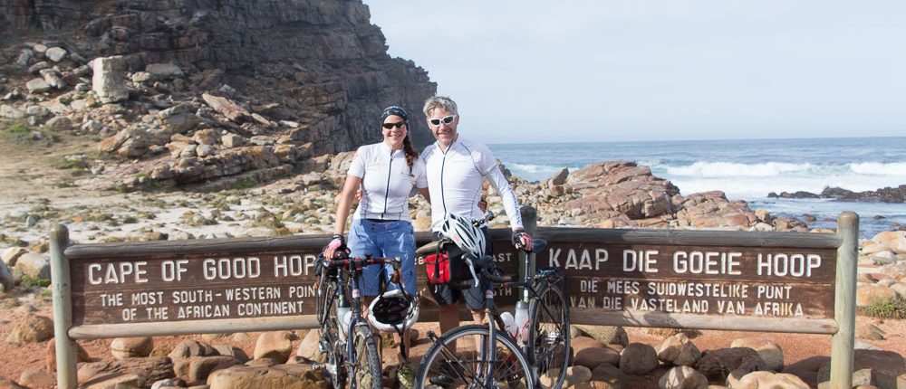 cycling-south-africa-western-cape-8280 This photo shows two adventure cyclists, Emily Conrad-Pickles and James Davis as they stand next to the famous sign at the Cape of Good Hope.