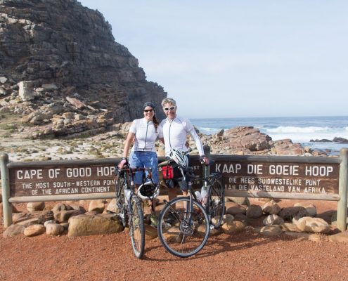 This photo shows two adventure cyclists, Emily Conrad-Pickles and James Davis as they stand next to the famous sign at the Cape of Good Hope.